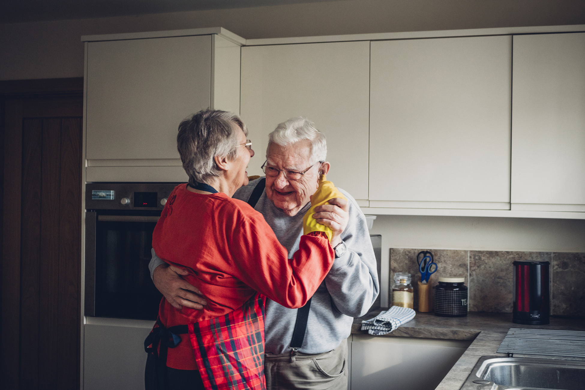 Elderly couple dancing in kitchen.