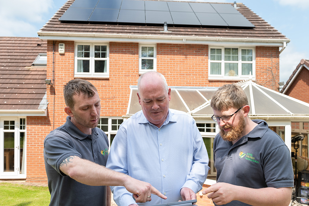 Installers with homeowner, in front of house with solar panels.