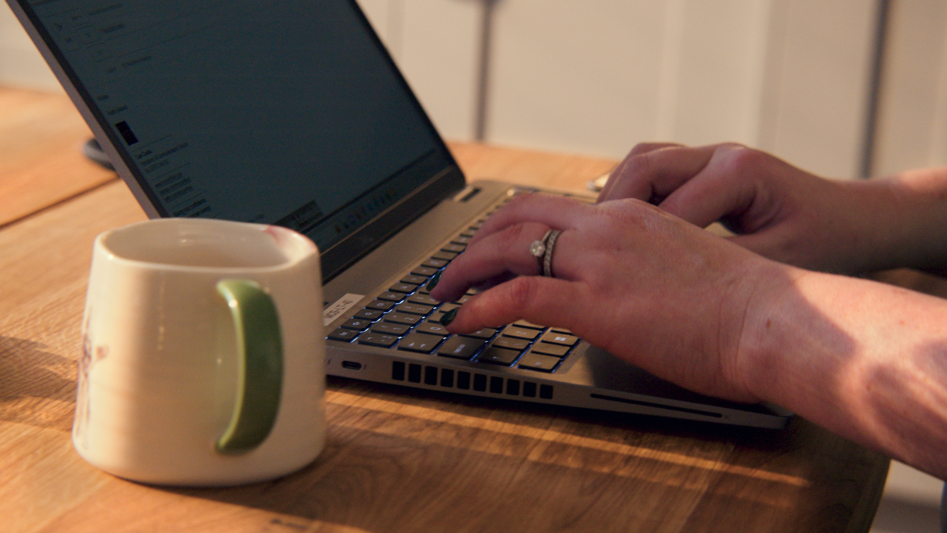 Typing on laptop with mug next to it.