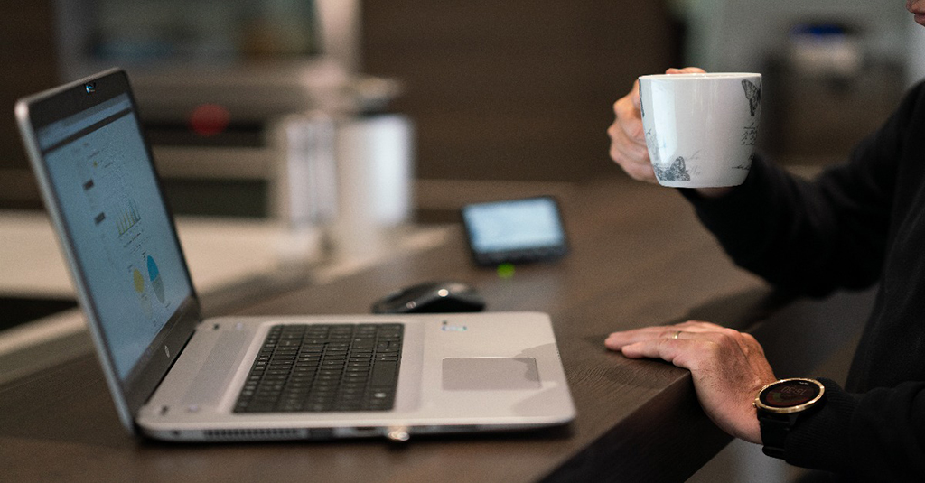Person on laptop holding mug.