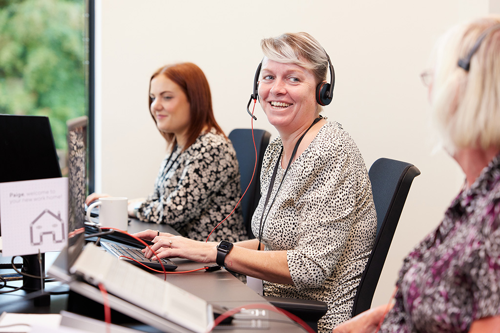 Women at desk with head sets on laughing.