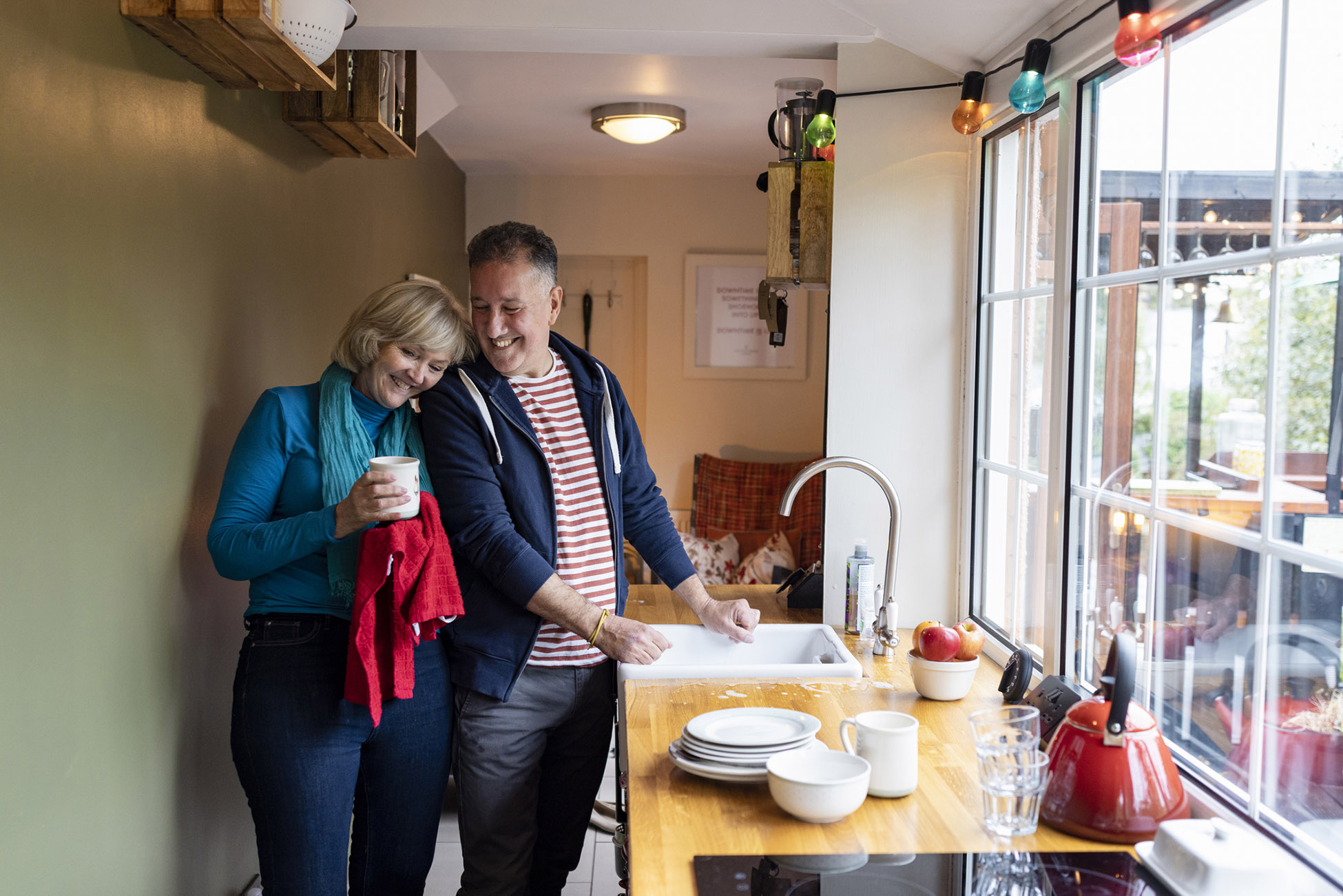 Couple washing dishes, drying off a mug.