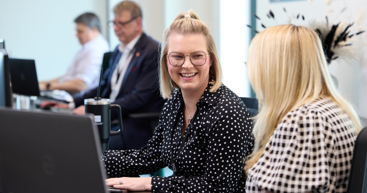 Two women sat at desk talking.