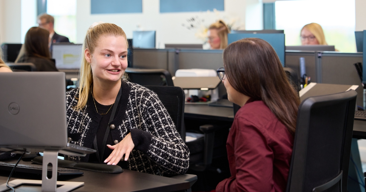 Two women sat at desk talking.