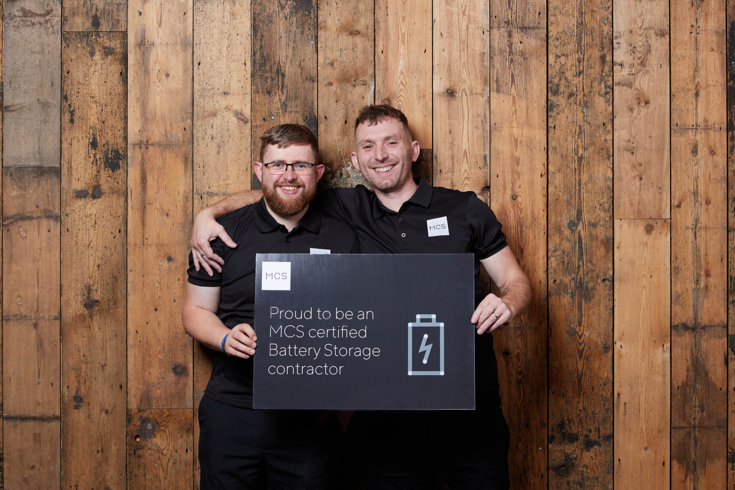 Installers holding a proud to be an MCS certified battery storage contractor sign.
