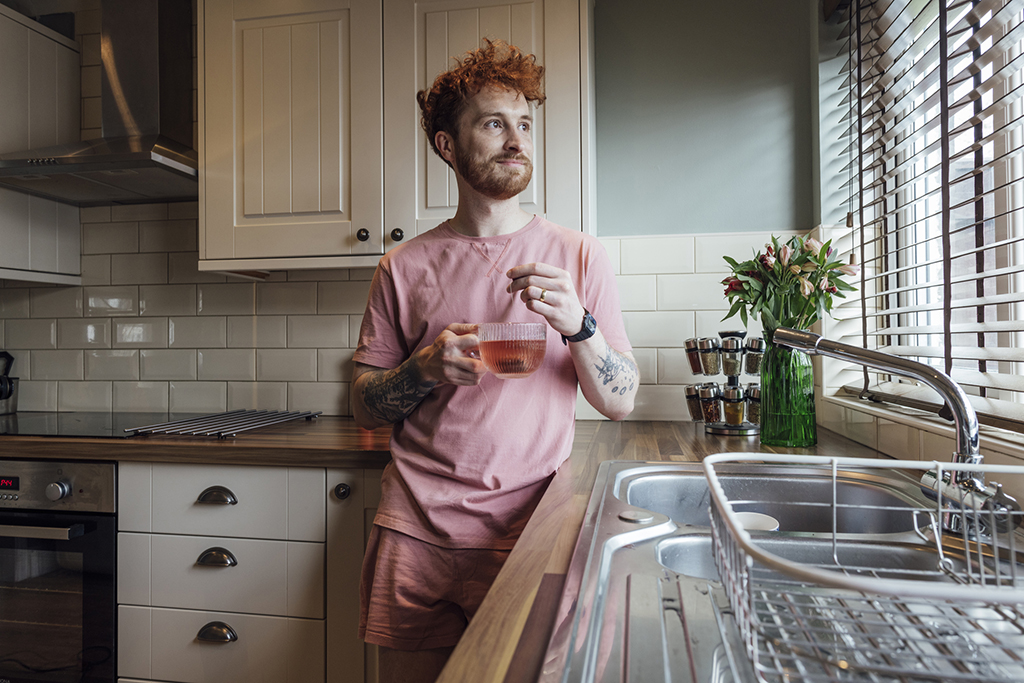 Man stood at sink with mug.