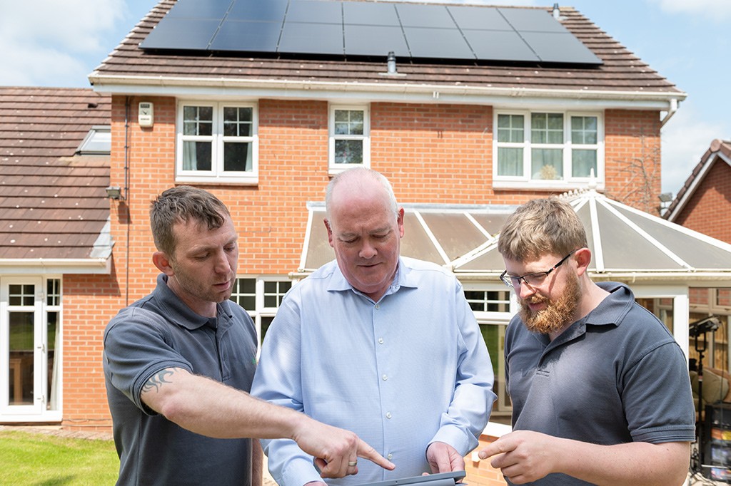 Installers and homeowner infront of house with solar panels.